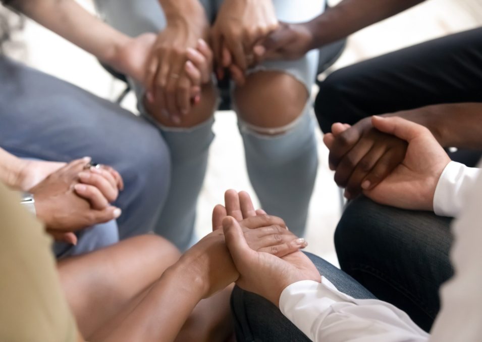Diverse people sitting in circle holding hands at group therapy session, religious christian team pray together for recovery give psychological support, counseling training trust concept, close up